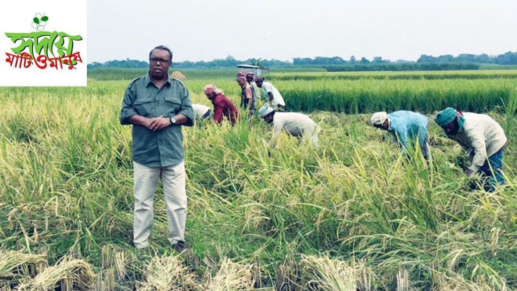 Shaikh Siraj is standing, with farmers harvesting rice in the background, depicting a scene from Shaikh Siraj and the 'Hridoye Mati O Manush' program.