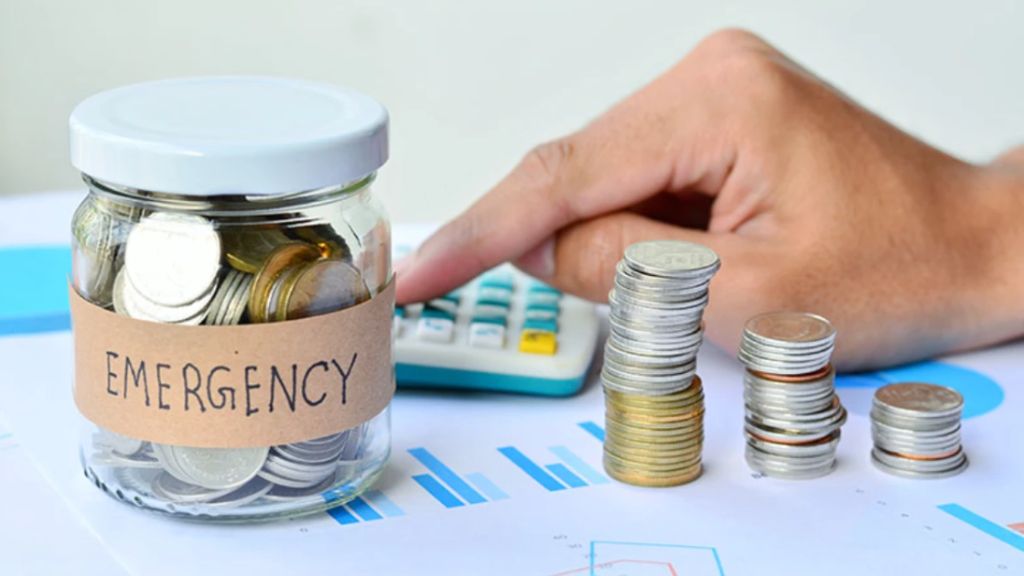 A person sitting at a table using a laptop and paperwork to coordinate savings and manage an emergency fund.